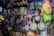 A variety of kitchen utensils and cleaning supplies are displayed on a densely packed store shelf. The items include colorful strainers, sponges, brooms, and packaged kitchen tools like spatulas and ladles. The display is vibrant with a mix of colors and textures.