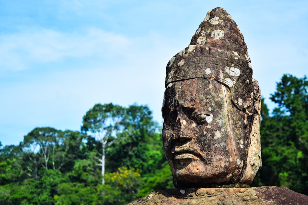 a stone statue of a head with trees in the background