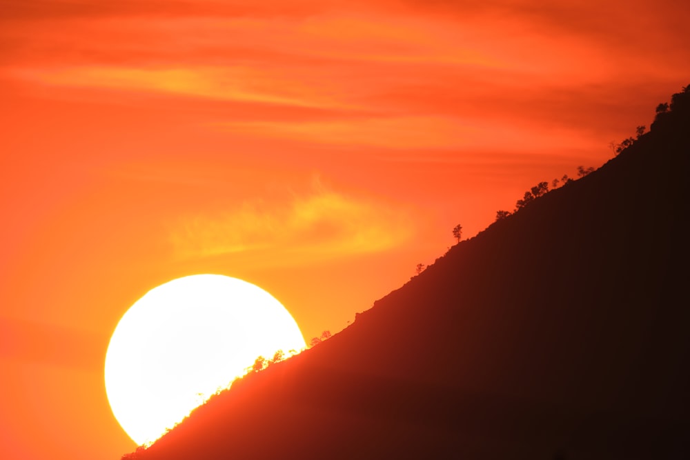 the sun is setting over a hill with trees on it