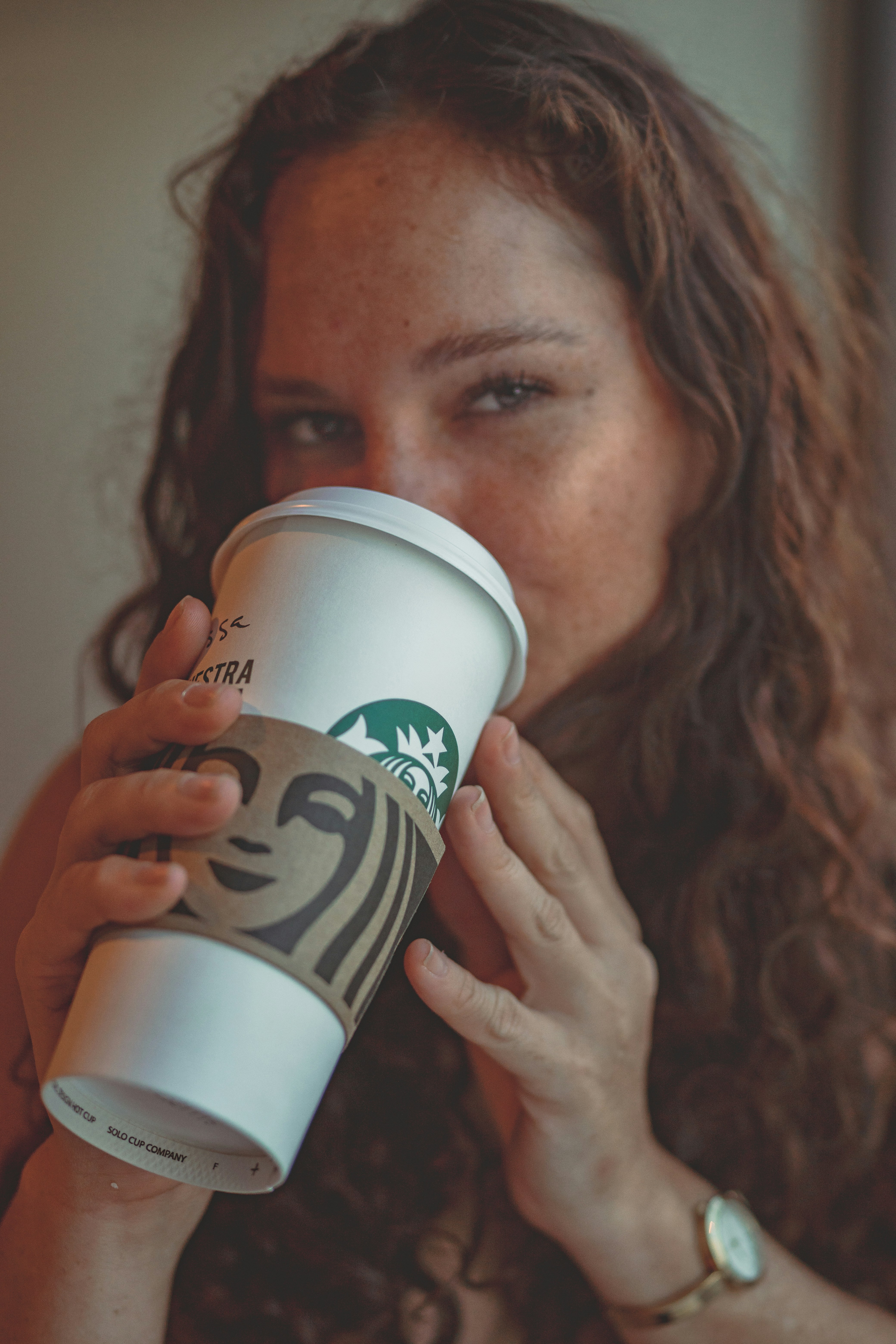 a woman drinking a starbucks coffee from a paper cup