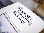 A white book cover with bold black text featuring the title 'The Photography Storytelling Workshop' by Finn Beales. The book is slightly tilted and occupies the foreground of the image.