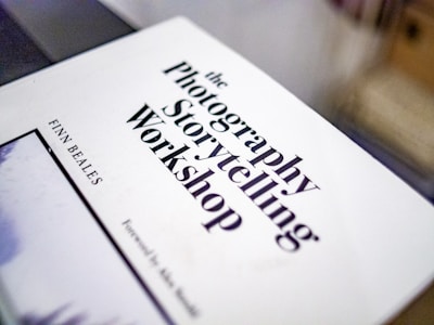A white book cover with bold black text featuring the title 'The Photography Storytelling Workshop' by Finn Beales. The book is slightly tilted and occupies the foreground of the image.