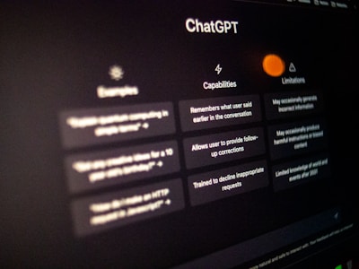 The image displays a computer screen interface of ChatGPT, showcasing different sections labeled as Examples, Capabilities, and Limitations. Each section contains brief explanatory text and an icon related to its function. The text appears slightly blurry due to the focus of the camera.