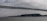 A large cargo ship labeled 'COSCO Shipping' is moving underneath a towering suspension bridge. The sky is overcast, creating a moody atmosphere. In the background, several small boats and a foggy city skyline enhance the scene.