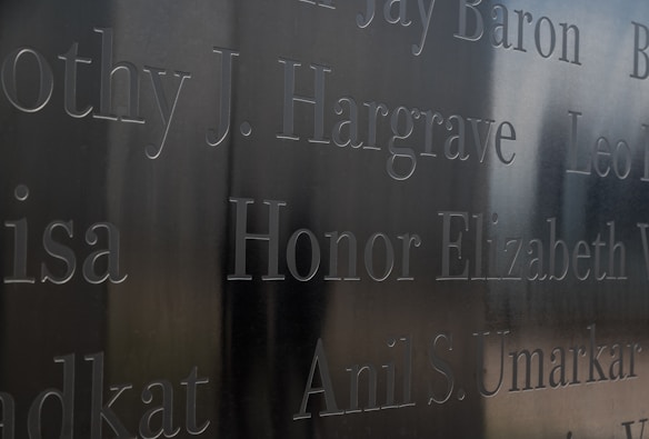 Names are engraved into a reflective metal surface, showing various names in a somber, memorial-like style. The engraving appears deep and is well-crafted, with a muted background reflection.