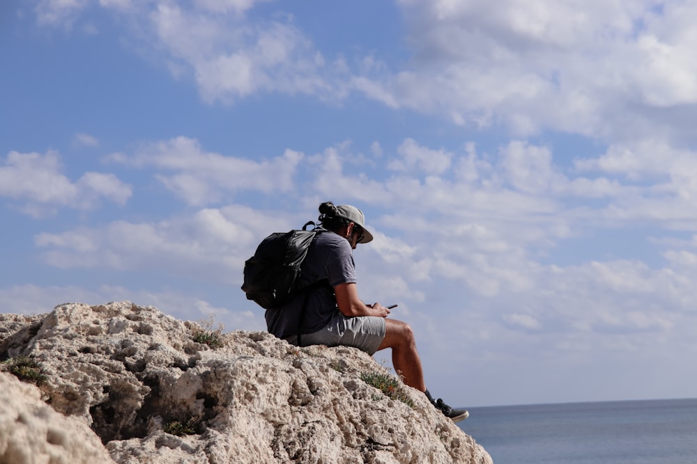a man sitting on top of a rock next to the ocean