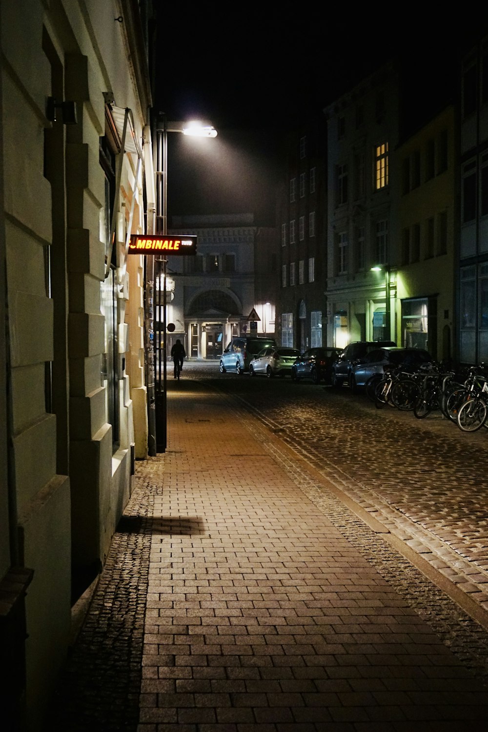 a cobblestone street at night with cars parked on the side of the street