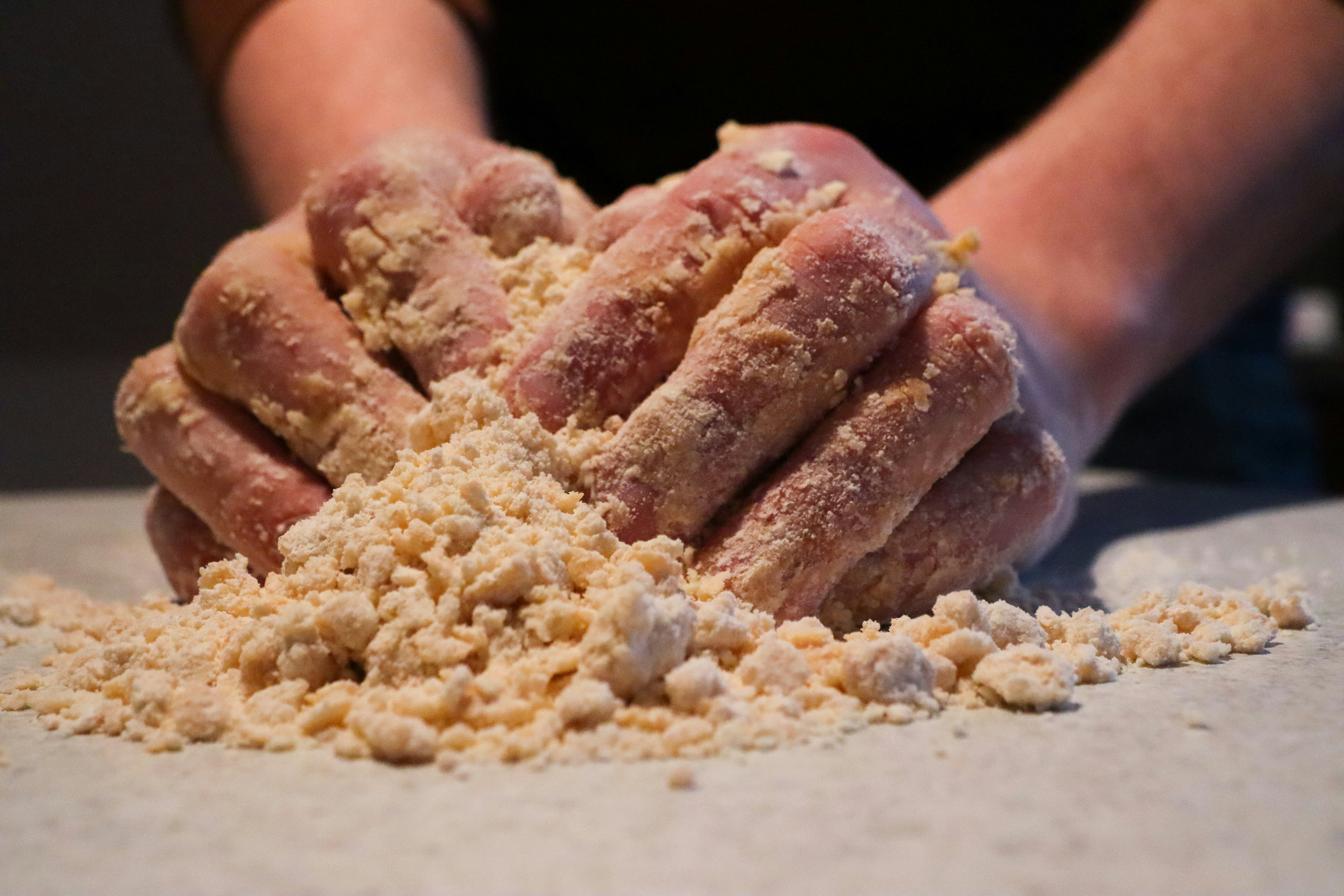 a person working with a pile of crumbly dough on a board