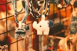 Two fabric animal keychains hang from a display rack. One is a white elephant with a blue tail, while the other is a smaller creature with a blue and white pattern. The background is warmly lit, with a blurred, golden bokeh effect.