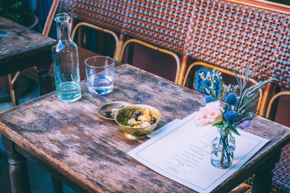 a wooden table topped with a bowl of fruit next to a vase of flowers