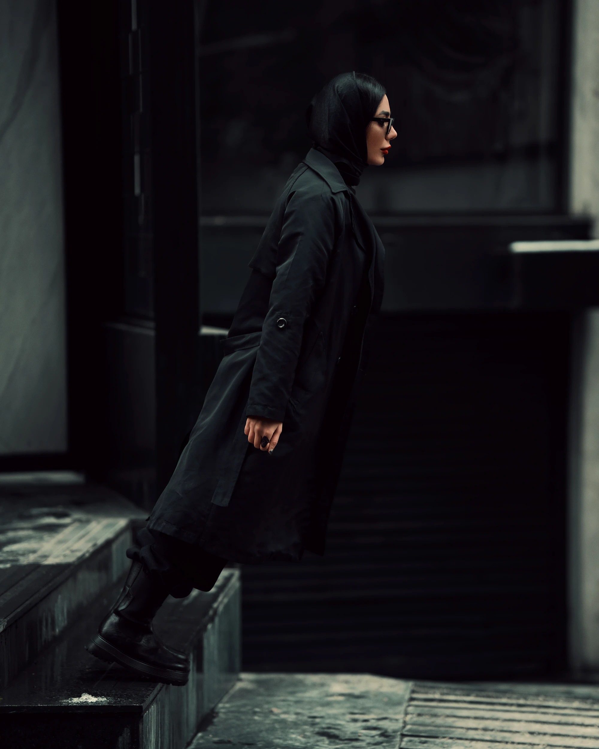 Model in a floor-length black coat walking down concrete steps