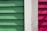 Wooden siding panels are arranged vertically in three distinct colors: green, white, and red. The texture of the wood is visible, with shadow patterns adding depth and contrast.