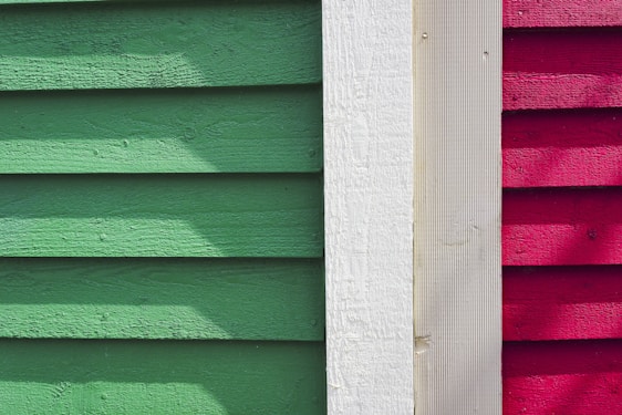 Wooden siding panels are arranged vertically in three distinct colors: green, white, and red. The texture of the wood is visible, with shadow patterns adding depth and contrast.