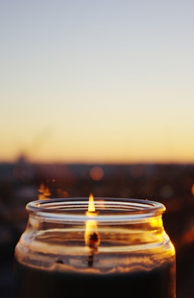 Close-up of a softly flickering soy candle in a rustic glass jar on a wooden table.