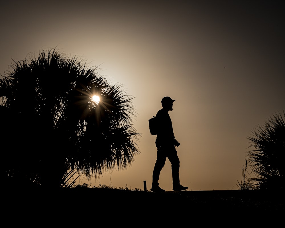 a silhouette of a man with a backpack walking towards the sun