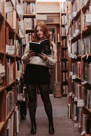 a woman standing in a library holding a book