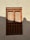 A traditional wooden window with an intricate design is set in a textured beige wall. The window has rectangular panels with circular metal studs and decorative cutouts at the bottom. Light and shadow play across the surface, casting a soft silhouette on the right side.