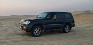A private luxury vehicle parked beside a desert dune under a golden sunset, ready for an excursion.