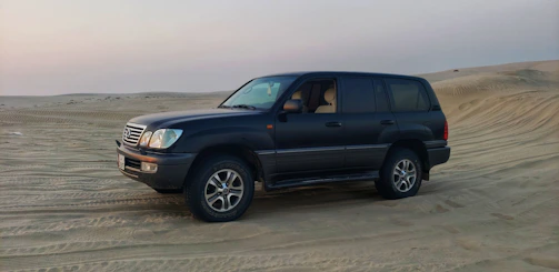 A luxury 4x4 vehicle parked beside the vast Sahara desert with a sunset backdrop.