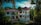 A luxurious two-story villa with a red-tiled roof surrounded by lush tropical greenery and tall palm trees. The building features white arches and a spacious balcony. A manicured garden and a cobblestone path enhance the scenery.