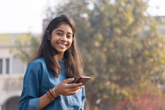 A young Indian woman smiling while holding her phone with a stylish dark navy phone skin, reflecting phonevibee.com’s bold design.