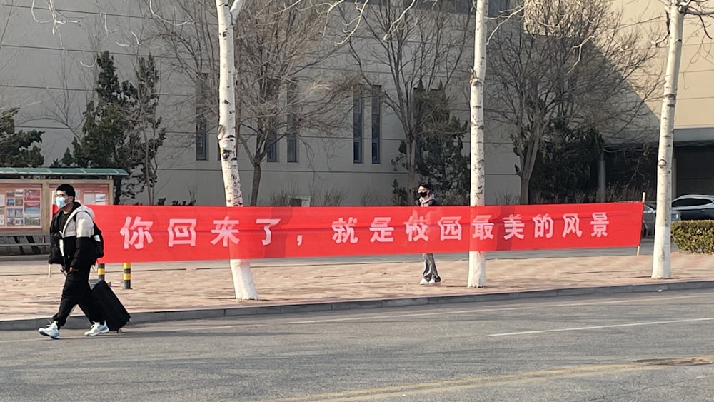 a man walking down a street past a red sign