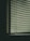 Horizontal blinds covering a window, with soft light filtering through, casting subtle shadows. The scene has a muted and slightly abstract feel, suggesting an indoor environment.