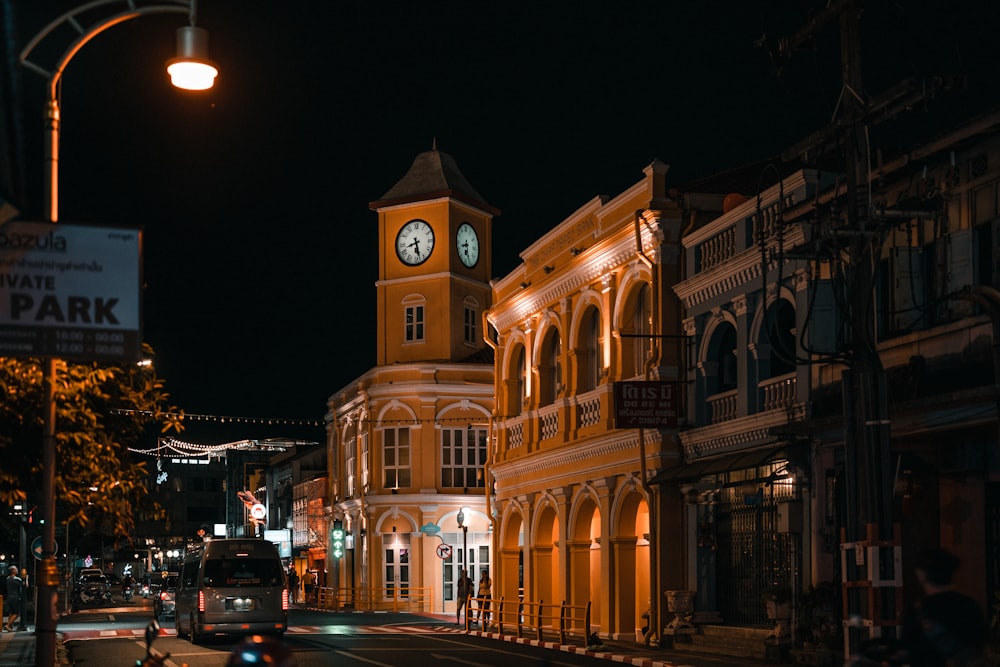uma rua da cidade à noite com uma torre do relógio ao fundo