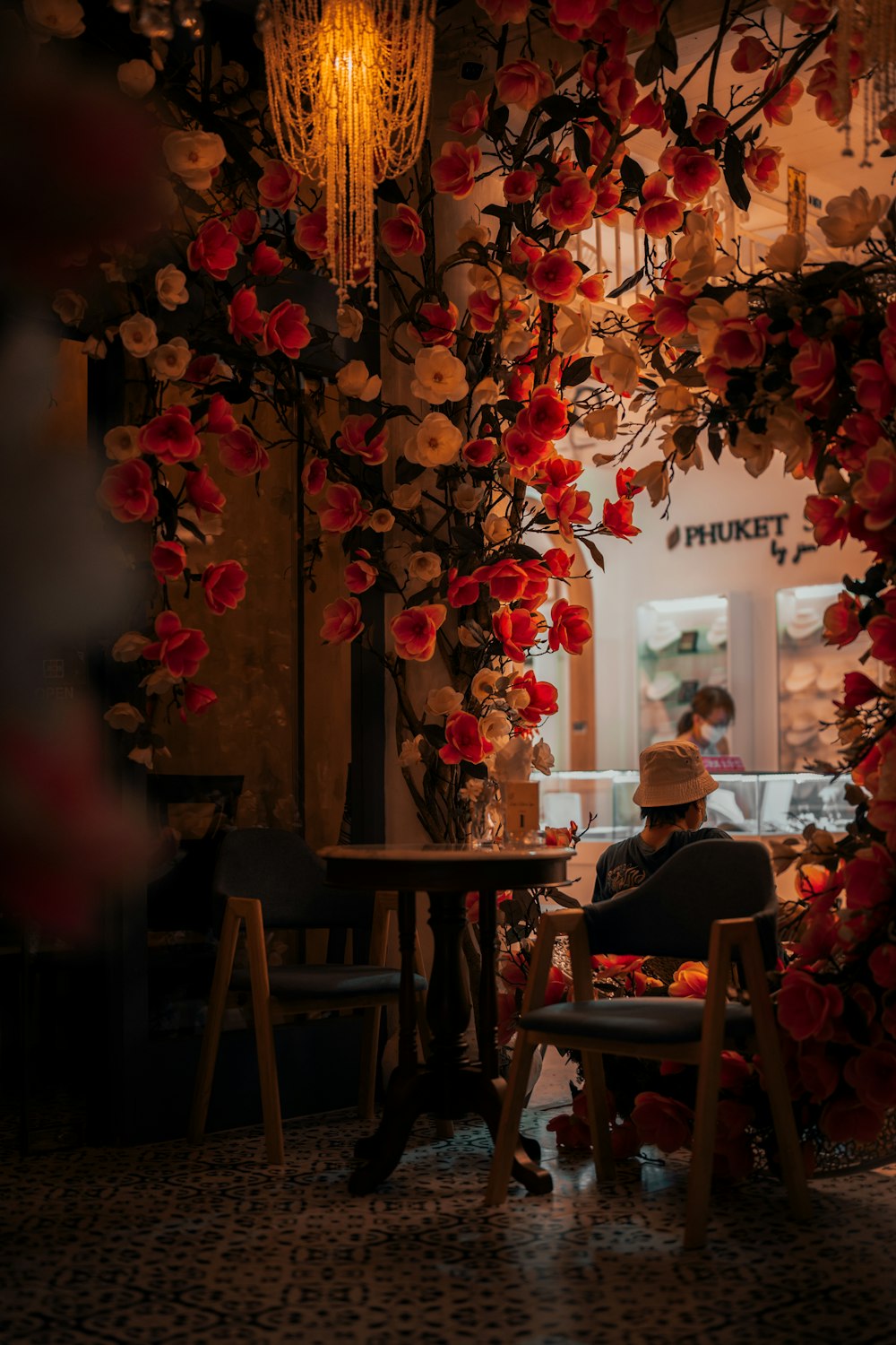 a man sitting at a table in front of a flower covered wall