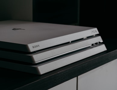 A close-up image of a Sony PlayStation 4 gaming console, featuring a sleek, tiered design with a matte finish and the Sony logo imprinted on the front.