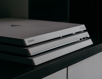 A close-up image of a Sony PlayStation 4 gaming console, featuring a sleek, tiered design with a matte finish and the Sony logo imprinted on the front.