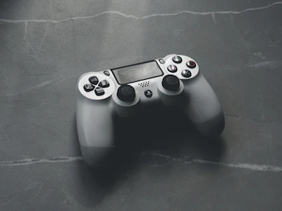 A sleek PlayStation controller resting on a table next to a snack and drink.