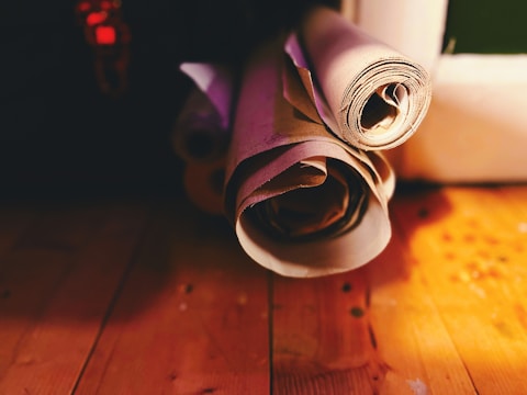 Several rolls of paper are placed on a wooden surface, bathed in warm light. Shadows and highlights create a cozy, vintage atmosphere.