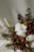 A detailed arrangement of dried flowers and plants, including green pine branches, brown leaves, fluffy white cotton, and small dried yellow buds. The natural textures and colors blend gently, suggesting a rustic and organic aesthetic.