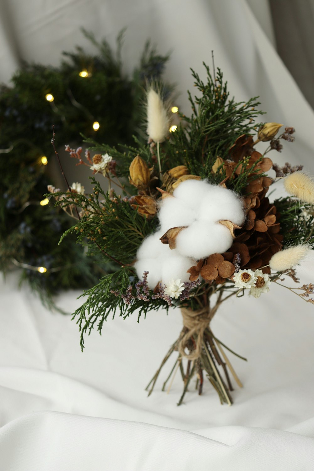 a bouquet of cotton, pine cones, and greenery