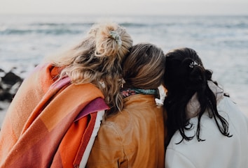 three women are sitting on a bench looking at the ocean