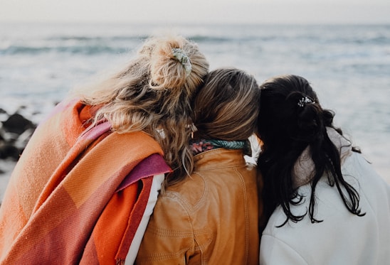 three women are sitting on a bench looking at the ocean
