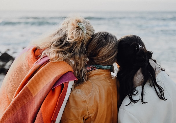 three women are sitting on a bench looking at the ocean