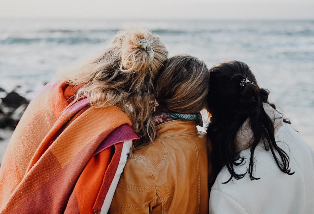 three women are sitting on a bench looking at the ocean