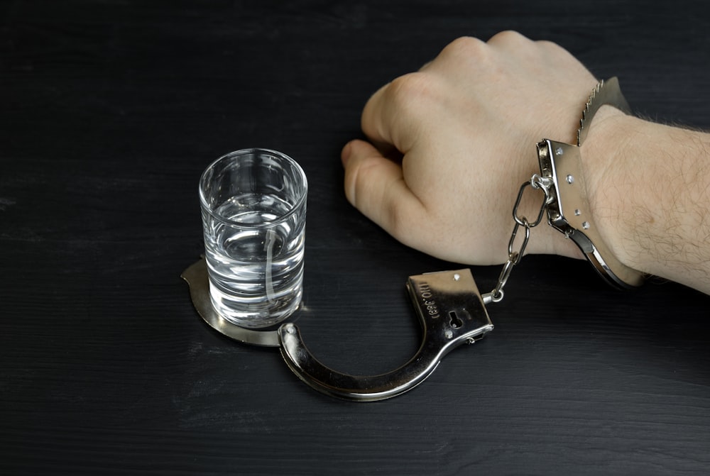 a man's hand with a handcuffs and a glass of water
