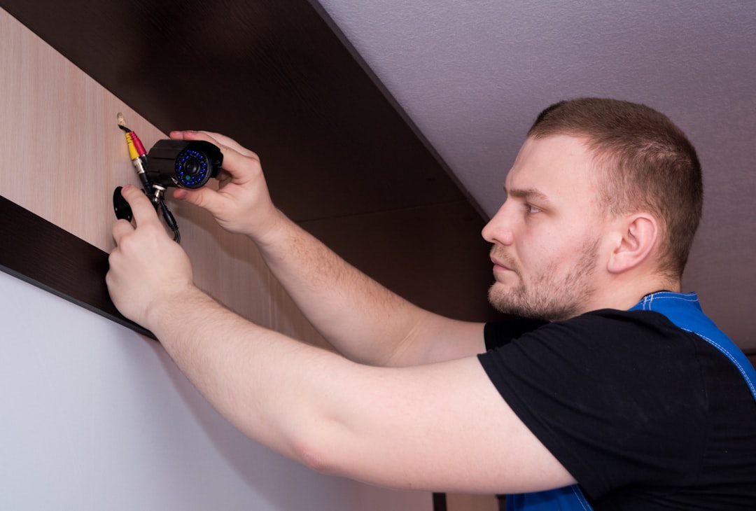 a man working on a wall with a screwdriver, Technician fixing video surveillance camera