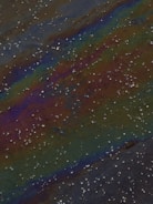 Close-up of oil slick spreading across calm water near a shoreline