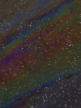 Close-up of oil slick spreading across calm water near a shoreline