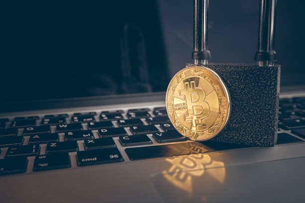 A golden Bitcoin coin is secured with a strong black padlock placed on top of a laptop keyboard with Russian layout. The image symbolizes security and protection in the context of digital currency.