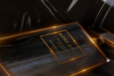 A perfume bottle with the label 'ROSE D'OR' visible, surrounded by a dark, reflective surface with warm highlights and light accents.