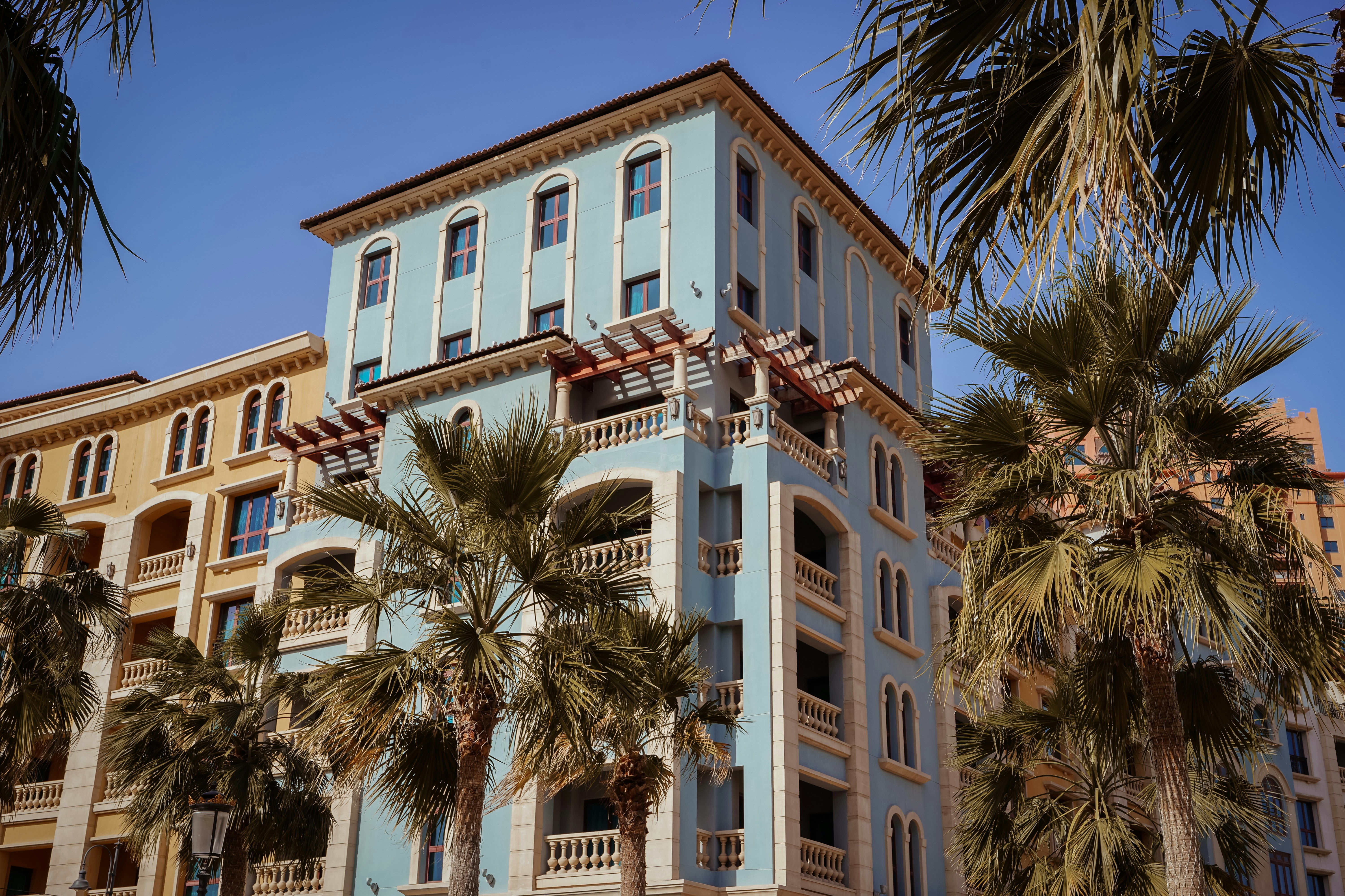 a tall blue building with palm trees in front of it, 