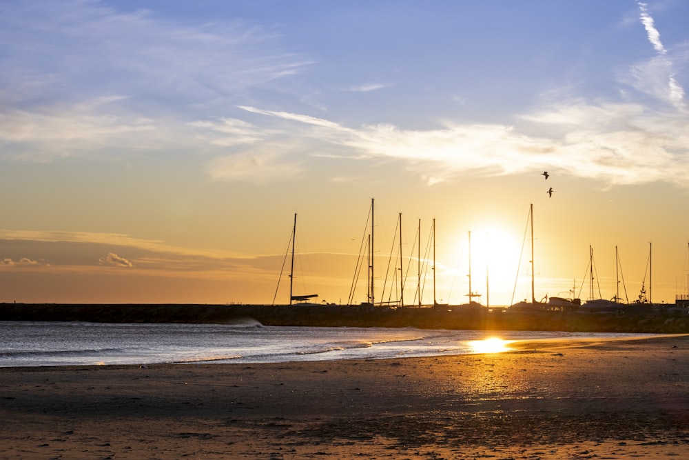 the sun is setting on the beach with sailboats in the background