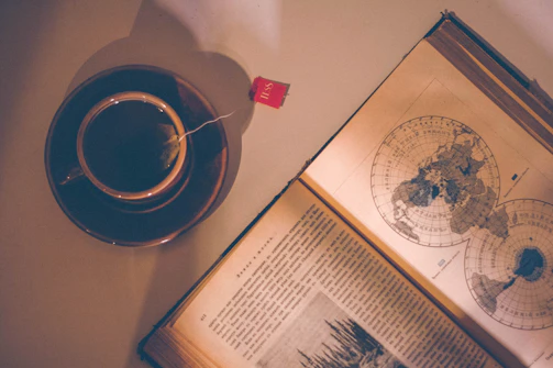 A cozy vintage suitcase with travel stickers, sitting beside a steaming cup of tea by a window.