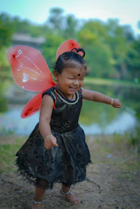 A joyful child wearing handmade paper wings smiling in a sunny park.