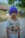 A child is wearing a colorful t-shirt featuring cartoon characters and a purple knit cap. The background shows blurred greenery and a rustic structure, suggesting an outdoor setting.